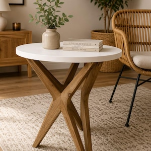 May include: A round side table with a smooth white circular top and a base constructed from four intersecting wooden legs. The table features a natural wood grain finish on the base and a clean white surface, providing a stable structure.