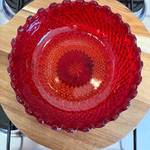May include: A vibrant red glass bowl featuring a detailed diamond-cut pattern across its surface. The bowl has a scalloped, serrated rim and a starburst design centred at the base, creating a textured appearance with light reflecting through the glass.