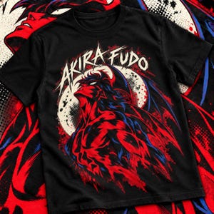 May include: A black short-sleeve t-shirt featuring a graphic print of a red and blue character with wings looking upward. The text AKIRA FUDO is printed in white above the character, set against a circular background with a dotted texture pattern.