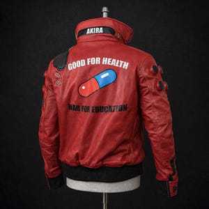 Pode incluir: Um casaco de couro vermelho com um gráfico de uma pílula vermelha e azul nas costas, com o texto branco "GOOD FOR HEALTH" acima e o texto preto "BAD FOR EDUCATION" abaixo. A gola exibe a palavra "AKIRA" em letras brancas.