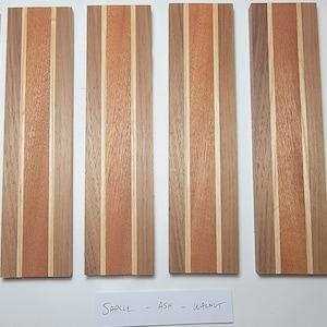 May include: Six wood samples with alternating stripes of light and dark wood. The samples are labeled "Sapelle", "Ash", and "Walnut".