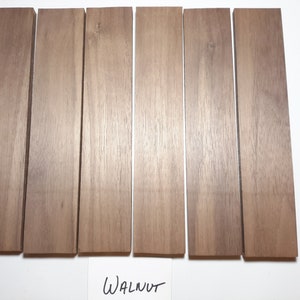 May include: Six pieces of walnut wood, each approximately 12 inches long and 1 inch wide. The wood is a light brown color with a natural grain pattern. The wood is labeled "WALNUT".