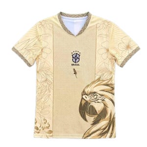 Może przedstawiać: Kremowy t-shirt z dekoltem w serek, posiadający środkowy panel w kropki, małą grafikę ptaka oraz herb Brasil z pięcioma gwiazdkami. Boki zdobią kwiatowe rysunki liniowe, a w prawym dolnym rogu znajduje się ilustracja dużej głowy papugi.