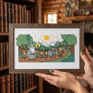 May include: A framed cross-stitch embroidery featuring a pixel art style scene of a group of fantasy characters walking along a path through a forest toward mountains under a yellow sun. The characters include a wizard with a staff and a shield-bearer.
