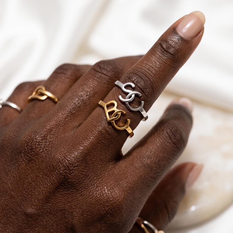 Dark-skinned hand wearing polished gold and silver custom two initial ring, elegant script initials