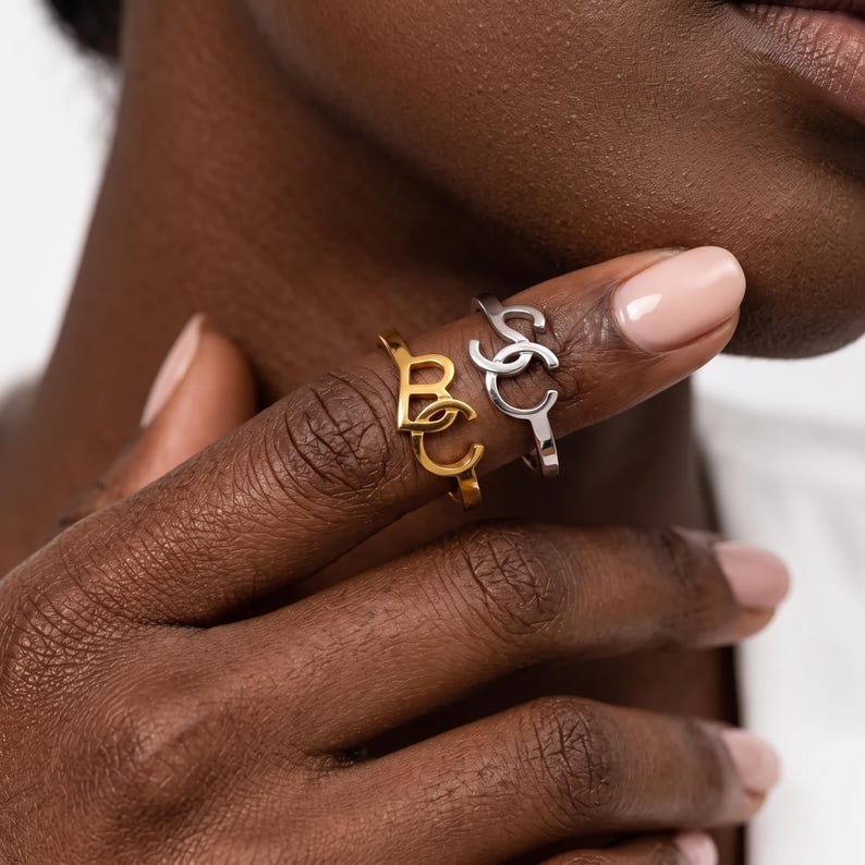 Close-up on fingers wearing mixed-metal custom two initial ring, overlapping scripted initials on polished bands