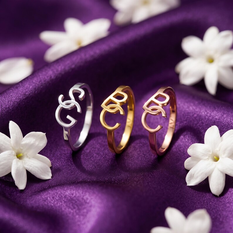 Three polished custom monogram rings arranged on purple fabric, interlocking initial ring choices in three tones