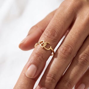Fair-skinned hand with rose-gold custom two initial ring, custom monogram ring on a slender open band