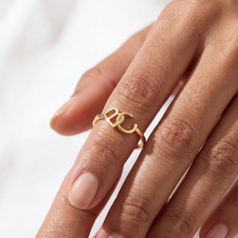 Fair-skinned hand with rose-gold custom two initial ring, custom monogram ring on a slender open band