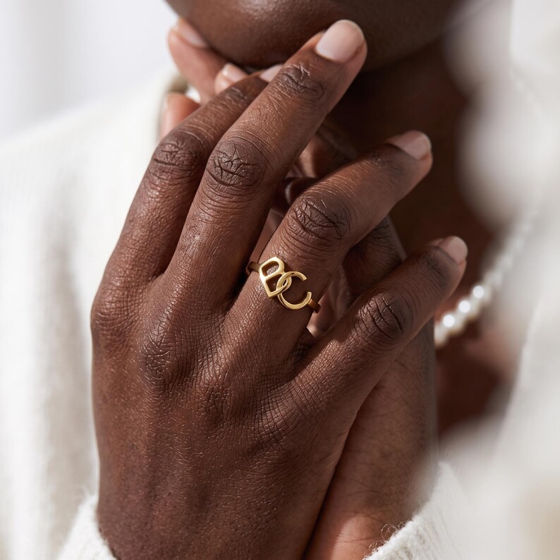 Paired hands styled with gold custom two initial ring, slim open-ended band, romantic couple initial ring vibe