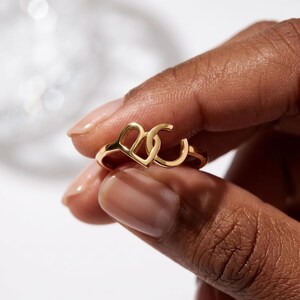 Fingers holding a rose-gold custom two initial ring, delicate script initials and polished open-ended band visible