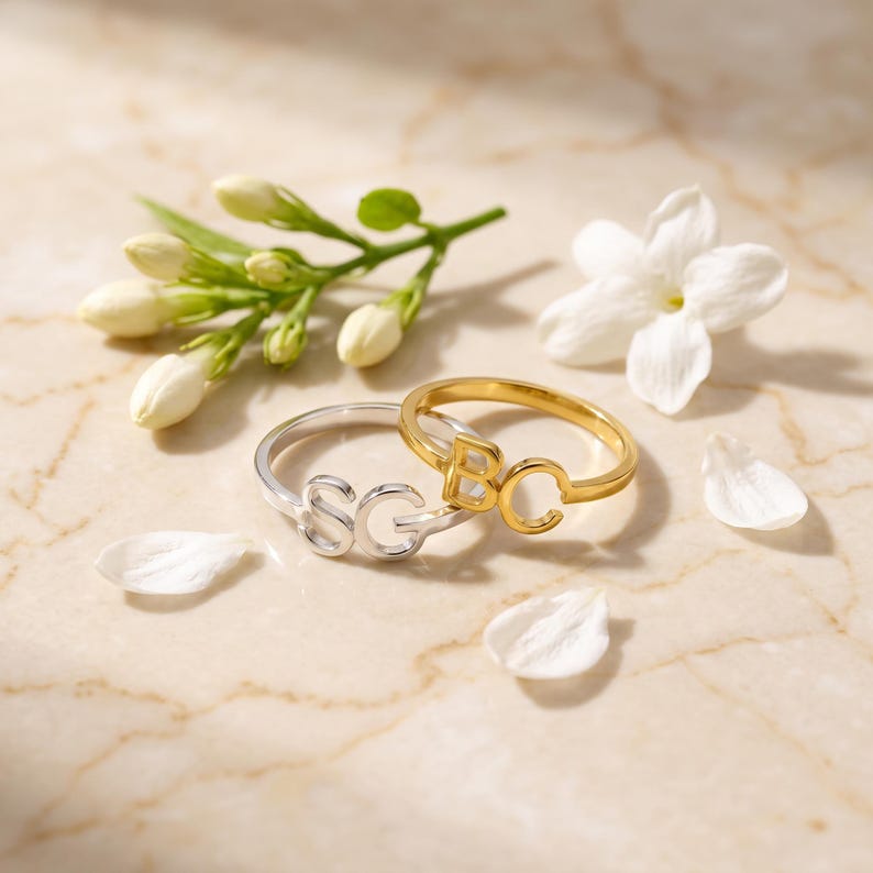 Gold and silver custom two initial rings on a marble slab with white blooms, elegant initial signet ring display