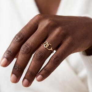 Hand wearing a slim gold custom two initial ring on middle finger, minimalist two letter ring look