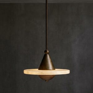 May include: A pendant light fixture featuring a dark bronze finish metal rod and a conical top piece. A flat, circular, translucent off-white stone disc sits horizontally, with a ribbed, dark bronze dome-shaped base attached underneath.