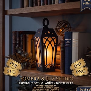 Può includere: Una lanterna in carta tagliata nera con ritagli a forma di arco e sagome di montagne alla base. La lanterna emette una calda luce arancione. Il testo sull'immagine include "best seller", "PDF", "SVG", "DXF", "PNG" e "SOMBRA & LUZ STUDIO".