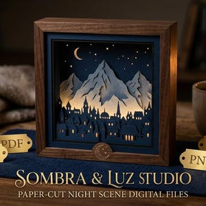 Puede incluir: Un marco de madera cuadrado que contiene una escena nocturna de papel recortado en capas con una cordillera y la silueta de una ciudad bajo una luna creciente y estrellas. Pequeñas etiquetas doradas con SVG, PDF, DXF y PNG están frente al marco.