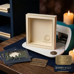 Puede incluir: Un marco de caja de sombra cuadrado de color crema con un logotipo dorado que muestra una luna creciente y estrellas. Junto a él, una manualidad de papel en capas representa un bosque con ciervos y osos. Dos etiquetas metálicas dicen SVG, PNG, DXF, PDF.