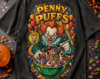 Puede incluir: Una camiseta gris carbón con lavado ácido que presenta un gráfico de un payaso con cabello naranja sosteniendo una cuchara sobre un tazón verde de cereales. El texto dice PENNY PUFFS y FREE. Los cereales son anillos de colores, ojos y calaveras.