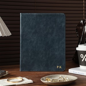May include: A dark blue rectangular portfolio case with a textured finish and the gold embossed initials P.K in the bottom right corner. The case features visible stitching along the edges and a slim, upright design suitable for holding documents.
