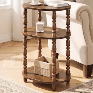 May include: A three-tier oval side table made of dark brown wood with turned spindle legs. The table features three smooth shelves supported by four vertical posts. A white cup, a book titled Cereal, a candle, and a woven basket are placed on it.