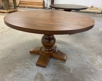 May include: A round wooden dining table with a dark brown finish. The table features a pedestal base with a decorative design and a smooth, circular tabletop. The table's diameter is approximately 48 inches.