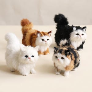 May include: Four plush cat figurines with fluffy fur. One is solid white, one is orange and white, one is black and white, and one is a calico pattern with black, orange, and white fur. Each cat has pointed ears, a small pink nose, and dark eyes.