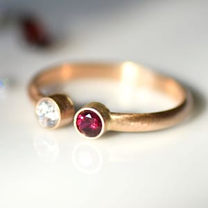 May include: A gold ring with a small white gemstone and a small red gemstone.