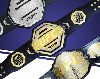 May include: Three championship belts with black leather straps. The top belt is silver with BMF text. The middle belt is gold with UFC text. The bottom belt is gold and silver with UFC Ultimate Fighting Championship text and side plates.