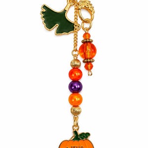 May include: A gold-toned metal keychain featuring a green ginkgo leaf charm, a dangling orange bead, and a vertical strand of orange, purple, and gold-toned beads. At the bottom hangs an orange pumpkin charm with the text Hello Pumpkin in black.