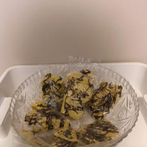 May include: A clear, decorative glass bowl with a scalloped rim containing several individual clear plastic bags. Each bag holds yellow, ridged potato chips that are drizzled with dark brown chocolate, creating a sweet and savory snack combination.