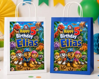 May include: Two rectangular paper gift bags, one white and one blue, each featuring a printed graphic of Paw Patrol characters, a red number 5, and the text Happy 5th Birthday Elias. The bags have white paper handles and a jungle-themed background.