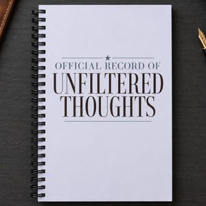 May include: A white spiral-bound notebook with black text on the cover that reads OFFICIAL RECORD OF UNFILTERED THOUGHTS, featuring a small star above the text. The notebook has a black metal coil binding along the left side for page turning.