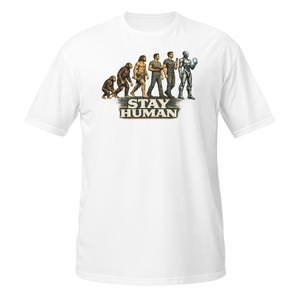 May include: A white short-sleeved t-shirt featuring a graphic print of human evolution progressing from a primate to a modern human and finally to a robot. Below the figures, the text STAY HUMAN is printed in a bold, dark, distressed font.