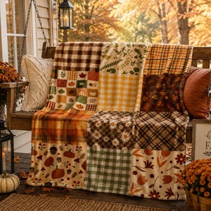 Könnte beinhalten: Eine Patchwork-Decke mit verschiedenen herbstlichen Mustern, darunter braun-weißes Karomuster, orange-gelbes Vichy-Muster, Kürbisse, Eicheln, Pilze, Gänseblümchen und herbstliches Laub in den Farben Orange, Braun und Grün.