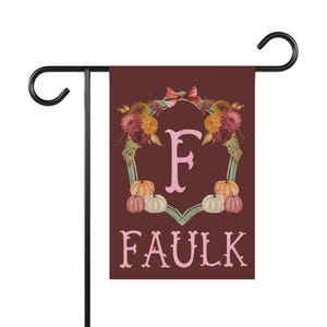 Peut inclure: Un drapeau de jardin rectangulaire sur fond bordeaux foncé avec une lettre F rose clair au centre et le nom FAULK écrit en rose clair en dessous. Une couronne florale composée de fleurs orange et rouges et de petites citrouilles entoure le F.