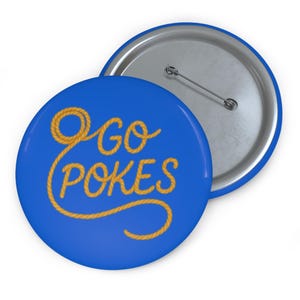 May include: A round pin-back button with a bright blue background. The text GO POKES is written in a yellow, rope-like font. The rope design forms a loop at the top and curves underneath the text. The back of the button is silver with a metal pin.