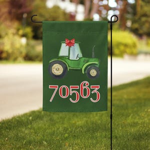 Op de afbeelding: Een donkergroene tuinvlag met een illustratie van een groene tractor met een rode strik op het dak. Onder de tractor staat het getal 70563 in een groot, wit lettertype met een rode omlijning. De vlag hangt aan een zwarte metalen standaard.