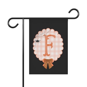 Peut inclure: Un drapeau de jardin noir avec un emblème circulaire festonné à motif vichy rose clair et blanc. La lettre F est centrée en orange, ornée d'une toile d'araignée et d'une petite araignée noire en haut à gauche, avec un nœud orange en bas.