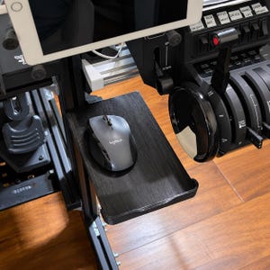 May include: A black Logitech computer mouse rests on a rectangular black textured tray attached to a flight simulator cockpit frame. The setup includes a black throttle quadrant with various switches and a tablet mounted above the mouse tray.