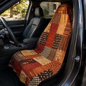 May include: A car seat cover featuring a patchwork design with various geometric and floral patterns in shades of deep red, burnt orange, tan, and dark brown. The fabric covers the entire front surface of the vehicle seat from headrest to base.