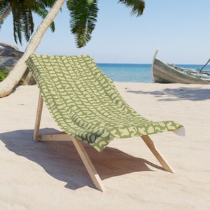 May include: A beach chair with a light wooden frame and a fabric seat featuring an olive green and cream-colored abstract pattern of repeating organic shapes. The chair is positioned at an angle, showcasing the backrest and seat surface clearly.