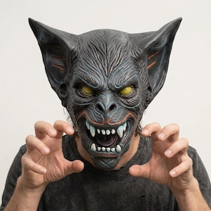 May include: A dark gray bat mask featuring large pointed ears, textured fur-like detailing, and piercing yellow eyes. The mask displays an open mouth with visible white fangs and sharp teeth, accented with subtle blue and orange highlights.