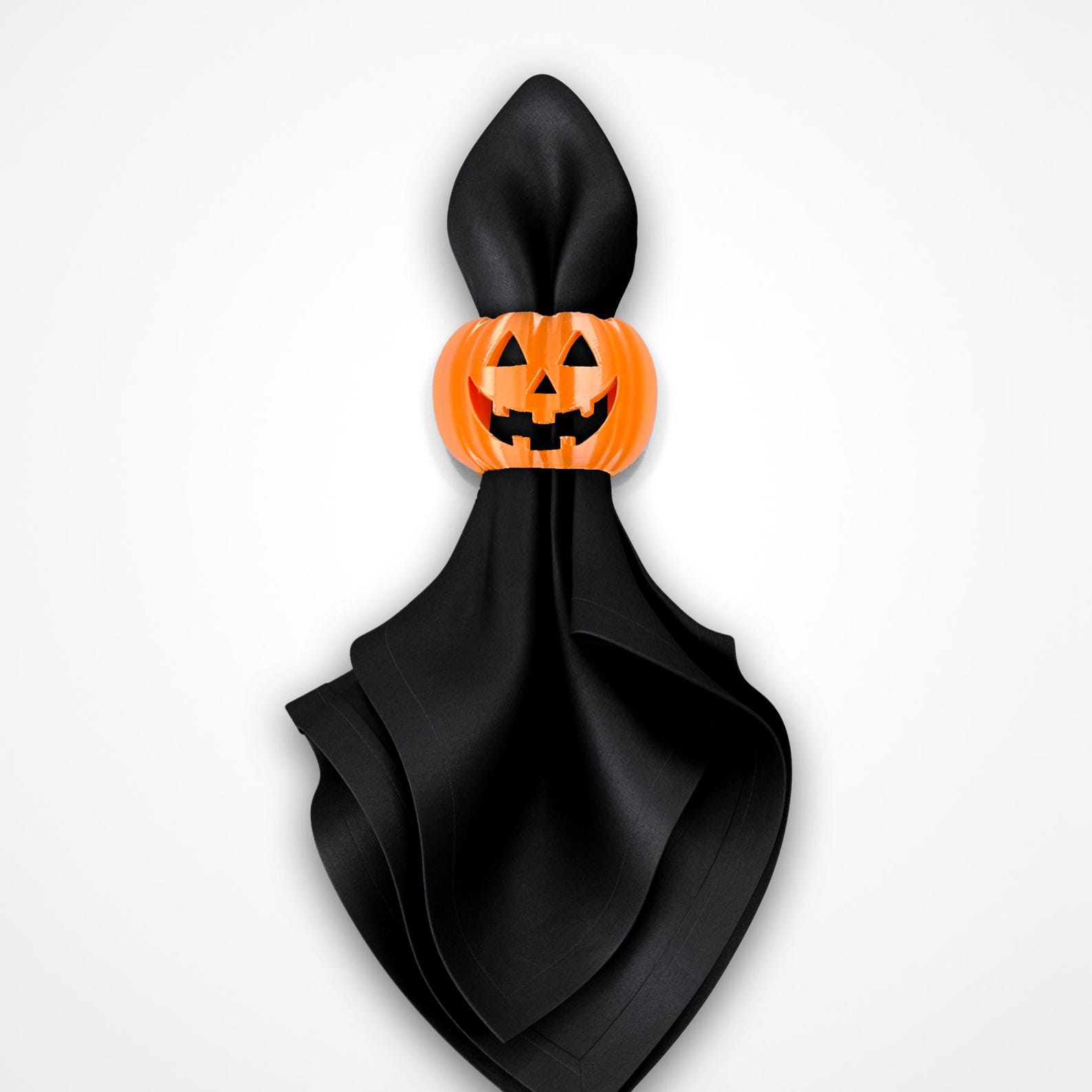 A Pointed Black Napkin with a Pumpkin Face Black cloth napkin gathered into points and held by an orange jack-o’-lantern ring.