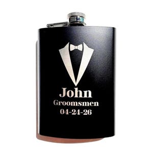 May include: A matte black metal flask featuring a silver engraved tuxedo jacket and bowtie graphic. The text reads John, Groomsmen, and 04-24-26. The flask has a silver screw-top cap with a textured grip and a hinged metal arm attachment.