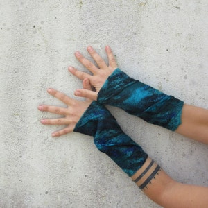 May include: A pair of teal blue fingerless arm warmers with a marbled pattern. The arm warmers are made of a soft, stretchy fabric.