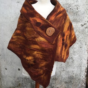 Puede incluir: Un chal de lana marrón y naranja con un botón de madera. El chal está drapeado sobre un maniquí blanco.