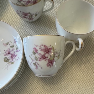 May include: White porcelain teacups and saucers with a floral design in shades of pink and green. The rims and handles are accented with gold trim. A classic tea set.