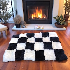 May include: A rectangular rug featuring a high-pile, shaggy texture arranged in a repeating black and white checkered pattern. The rug consists of alternating square blocks of solid black and solid white fibers, creating a bold, high-contrast design.