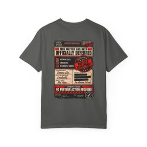 Könnte beinhalten: Ein anthrazitfarbenes T-Shirt mit einer Grafik auf der Rückseite, die einem offiziellen Verwaltungsformular ähnelt. Der Text lautet: This matter has been officially deferred, referred to another department, acknowledged, considered, deliberately ignored, someone else, eventually, not mine, und no further action required.