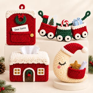 May include: A collection of four crocheted Christmas items: a red postbox with a Dear Santa note, a three-car train garland carrying gifts, a red house-shaped tissue box cover, and a cream-coloured crescent moon wearing a Santa hat with a pocket.